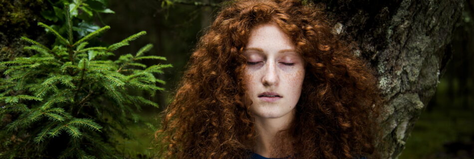 eine junge Frau steht mit geschlossenen Augen im Wald - Gewahrsein oder Achtsamkeit