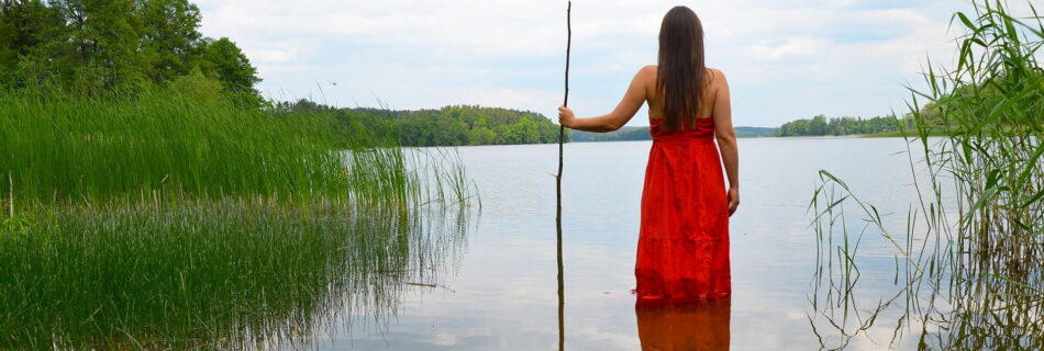 eine indigene Frau in einem roten Kleid steht am Rande eines Sees im flachen Wasser - Wasser energetisieren mit der Wasserlied der Algonquin-Nation